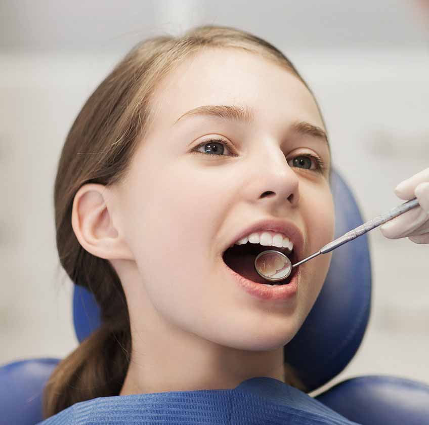 Zahnkontrolle mit Dentalspiegel bei einer jungen Patientin. 
