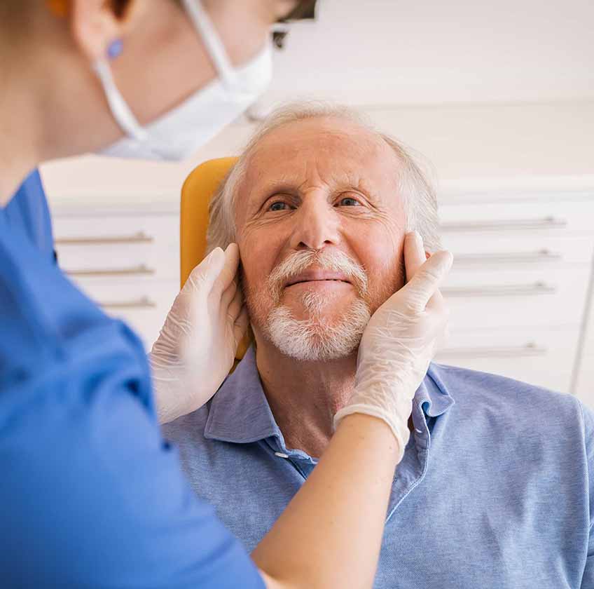 Zahnärztin tastet Kiefergelenke eines Patienten ab.